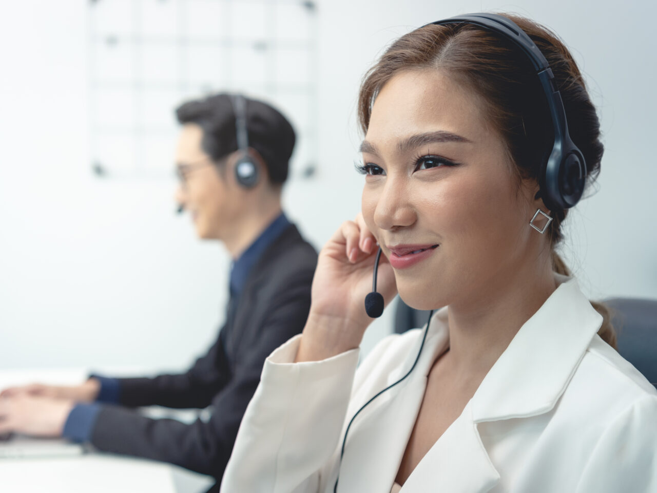 Asian call center agent team, customer service support wearing headset or headphone talking with customer in modern office.